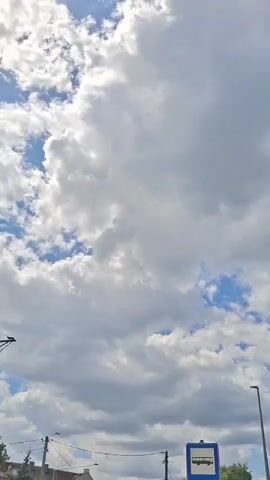 This video shows a view of the sky from a low angle. The sky is blue with white clouds. In the foreground, there is a bus stop sign. There are also power lines and a street light visible. The video appears to be shot outdoors on a sunny day.