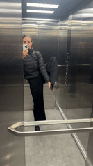 Woman Takes Elevator Selfies in Black Puffer Jacket