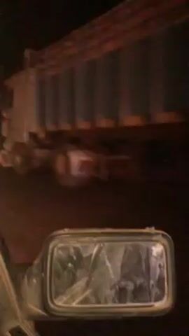 The video shows a dark, grainy scene from the perspective of a vehicle’s side mirror. Several large trucks pass by on a poorly lit road at night. The side mirror is cracked.  The trucks are moving quickly and are blurry, making it difficult to discern specific details about them.