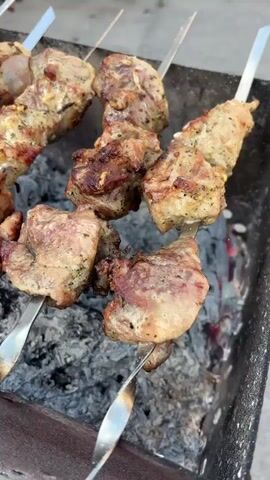 The video shows skewers of meat grilling over hot coals. The meat appears to be pork or lamb, cut into bite-sized pieces and seasoned with spices. The skewers are placed on a metal grill, and the coals are glowing red and emitting heat. The video is shot from a close-up perspective, focusing on the details of the grilling meat and the fire.