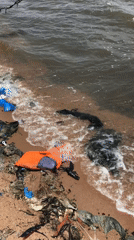 Waterfront area shows environmental decay, abandoned boats, scattered debris