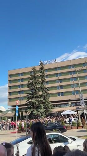 Crowd gathers behind barricades in Pernik to observe passing vehicle