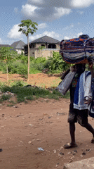 Person carries textiles on head along dirt road in Nkpor