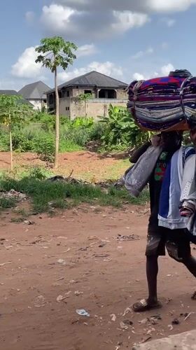 Person carries textiles on head along dirt road in Nkpor