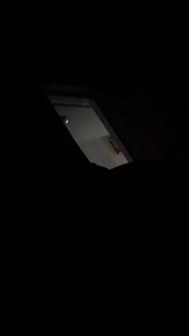The video shows a dark room with a skylight. Through the skylight, a dimly lit room with a wooden surface is visible. There is a faint light source in the room.
