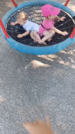Two kids laughing on a nest swing in an Olomouc park