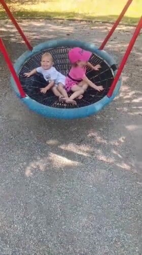 Two kids laughing on a nest swing in an Olomouc park