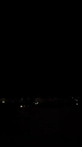 The video begins with a view of a dark night sky over a distant cityscape, with faint lights visible. Suddenly, a bright flash of lightning illuminates the clouds, revealing a stormy sky. The video then returns to darkness, showing the distant lights of the city again.