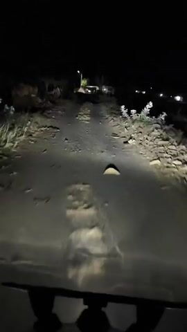 The video shows a first-person perspective of driving a vehicle at night on a bumpy dirt road. The headlights illuminate the rough terrain ahead, with rocks and uneven patches visible. The darkness surrounding the road suggests a rural or undeveloped area. There are no other vehicles or people clearly visible in the footage. The camera appears to be mounted inside the vehicle, possibly on the dashboard or windshield.