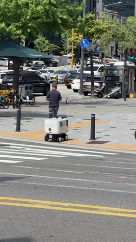 Sidewalk delivery robot navigates Seoul streets alongside pedestrians.