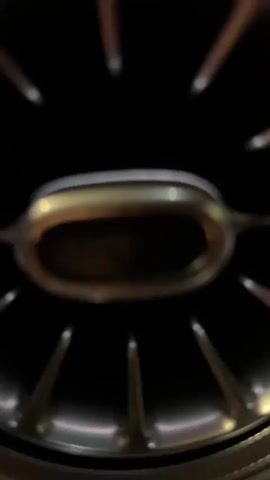 This is a video clip featuring a close-up view of a car's interior air vent. The vent is circular with a metallic finish, featuring radiating spokes and an oval-shaped opening in the center. The opening itself has a textured interior, suggesting it's a functional vent for air circulation. The surrounding dashboard material appears to be dark and matte, with some subtle reflections indicating artificial lighting. Below the vent, a chrome-finished knob or dial is partially visible, likely controlling the vent's function.

The camera appears to be stationary, with slight focus adjustments to highlight different parts of the vent. The lighting is dim, characteristic of an indoor setting or nighttime driving. No people are visible in the frame. The overall impression is one of a modern and potentially luxurious vehicle interior, with a focus on the design details of the climate control system. There is no discernible text in the video. The location context of Berlin, Germany, does not provide any specific visual cues within the frame itself, as the interior of a car is generally standardized across locations.