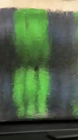 The video shows a close-up view of a car wash's scrubbing brushes. The brushes are bright green and appear to be rotating or moving up and down. The view is somewhat obscured by water and soap. The background is dark and out of focus.