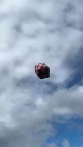 A red and white checkered sky lantern floats against a cloudy sky. Smoke is visible from the bottom of the lantern.