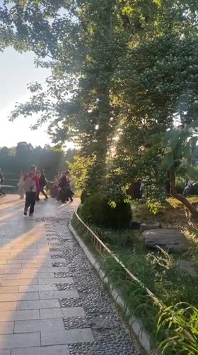 People walk along waterside stone pathway in Beijing park