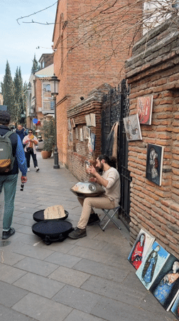 Street musician plays handpan on decorated Tbilisi sidewalk