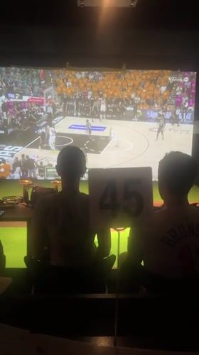 Two people watch basketball on big screen in NYC venue