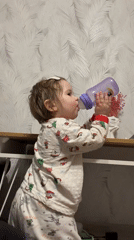 Child in Christmas pajamas drinks from purple bottle