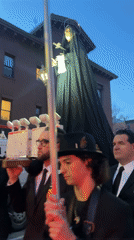 Religious statue procession observed on urban street at dusk