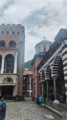 Visitor documents Rila Monastery's architecture and grounds under cloudy skies