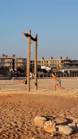 Quarteira beach at golden hour: swings, paddleboards, and a passing vessel