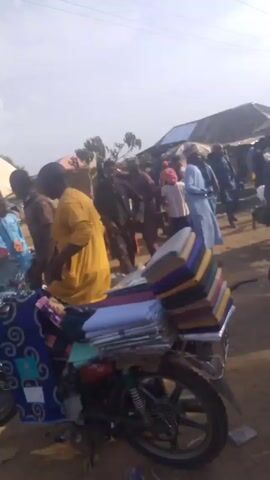 The video depicts an outdoor market setting with numerous individuals. Many people are dressed in traditional clothing. Some vendors have set up stalls under umbrellas. The ground is dirt, and there is visible litter. People are shopping, browsing merchandise, and walking through the market. A woman carrying a child on her back is visible in the first shot. The video gives a sense of a busy and lively market atmosphere.