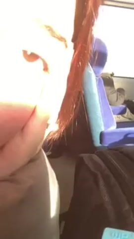 The video shows a close-up view of a person's face, specifically focusing on their eye and cheek. The person has reddish-brown hair. They are sitting on what appears to be a train, indicated by the blue seats and the presence of other passengers in the background. A black bag is also visible nearby. The scene is brightly lit, possibly due to sunlight coming through the train windows. The person appears to be holding the camera close to their face.