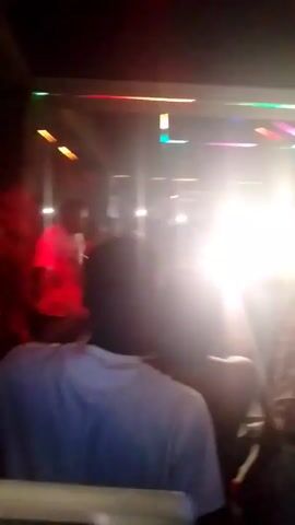 The video appears to be taken inside a crowded nightclub or party venue. There are many people, their faces obscured by bright lights and movement. The lighting is colorful, with lasers and spotlights in various shades of green, blue, pink, and white flashing around the room. People appear to be dancing or socializing, although specific actions are hard to discern. The overall atmosphere seems lively and energetic.
