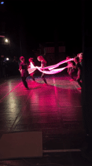 Dance troupe performs with white cloth on pink-lit stage