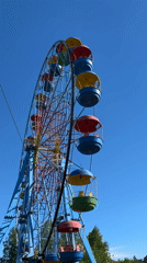 Park visitors enjoy Ferris wheel, skatepark, playground on sunny afternoon