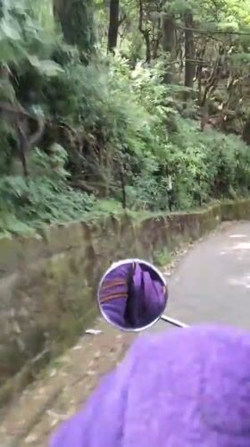 Motorcyclist in purple jacket rides paved road in Dharamkot