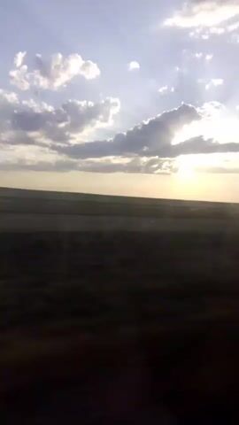 The video shows a time-lapse of clouds in the sky with the sun shining through them. The sun is low on the horizon, suggesting it is either sunrise or sunset. There is a vast, flat expanse of land visible below the sky. The overall impression is one of natural beauty and serenity.