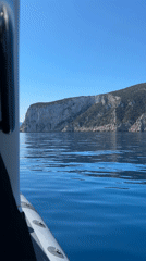 Boat travels past rocky cliff in calm Italian waters