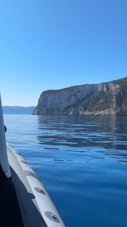 Boat travels past rocky cliff in calm Italian waters