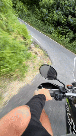 Motorcycle rider travels scenic Kintamani road, encounters yellow truck