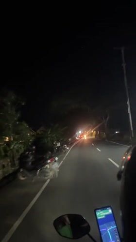 Motorcycle rider navigates dark road in Mengwi, Indonesia