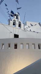 Greek flags line a white bell tower in Thira