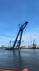 Crane barge and tall ship share Gdańsk harbor on a clear morning