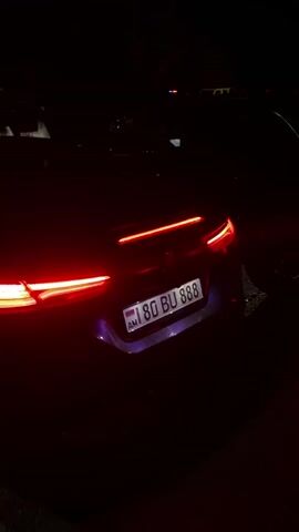 The video shows a nighttime scene focused on a purple convertible car with Armenian license plates. The car's rear lights are illuminated, and the video pans to reveal the side profile of the vehicle. The interior dashboard screen is visible. Other cars are parked in the background, and a few people are seen standing nearby. The environment appears to be a parking lot or gathering area at night.