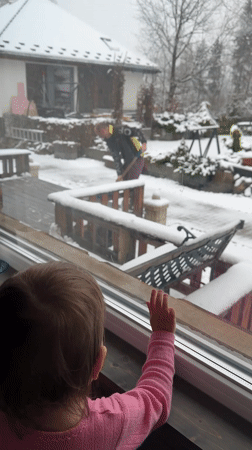 Child watches snow shoveling from window in Wisła