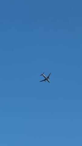 An airplane is flying in a clear blue sky. The airplane is a commercial jet with two engines visible under the wings. The airplane is angled slightly upwards and to the right. The sky is a solid, uniform blue with no clouds.