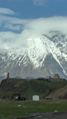 Historical stone tower filmed against snow-capped mountain backdrop in Georgia