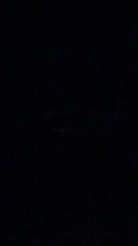 The video is shot at night in what appears to be a very dark environment. Initially, a red light or lights are visible in the center of the frame. These lights briefly disappear, and then a green light appears near the lower right corner of the frame. The overall setting suggests a night sky or a dark, outdoor space.