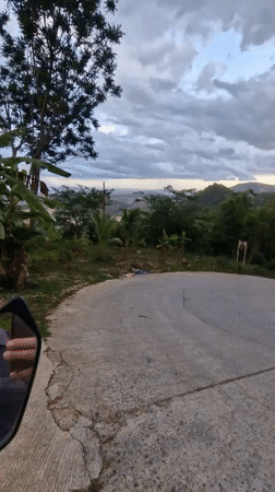 Motorcyclist navigates worn road amid lush vegetation, litter in Ko Samui