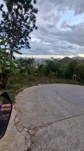Motorcyclist navigates worn road amid lush vegetation, litter in Ko Samui