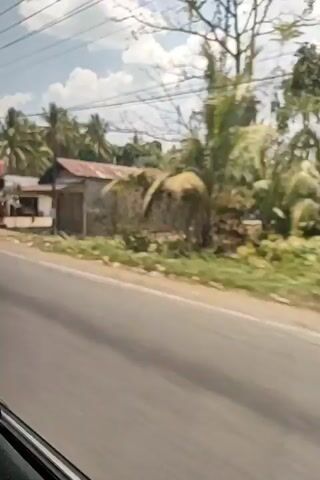 A blurry video shows a red truck driving on a road next to several buildings. The truck is in the foreground, and the buildings are in the background. The sky is blue with some clouds. There are power lines running across the top of the frame. The video is shaky, suggesting it was filmed from a moving vehicle.