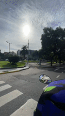 Scooter rider travels tree-lined Buenos Aires street under hazy skies