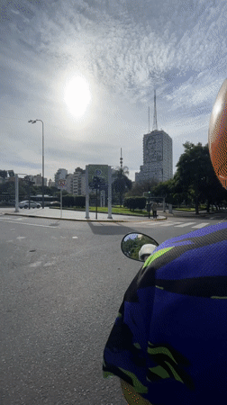 Scooter rider travels tree-lined Buenos Aires street under hazy skies