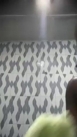 Here's a description of the video:

A person stands in a shower with a tiled wall behind them. They are wearing a bright green exfoliating glove on their hand and are rubbing their hands together, creating a lather of white soap.
