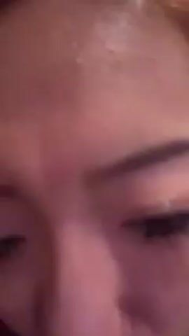 The video begins with a close-up shot focused on an individual's face, possibly the person holding the camera. The view then shifts to a wider angle, revealing a young woman with reddish-orange hair and fair skin. She is wearing a black top with a cutout design near the collar and is seated inside what appears to be a restaurant or bar with dark wood paneling. In the background, there's a floral arrangement featuring red roses and green foliage. The woman looks directly at the camera, briefly moves her hands, and makes a funny face. The video ends.