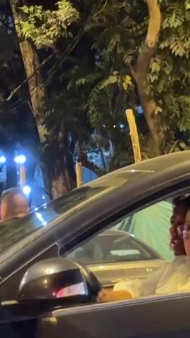 A mobile phone video shows an occupied car at a closed-off street. In the low-light video, police barricades are set up across a street with a sign that reads "Calle Clausurada", meaning street closed. There are pedestrians in the background.  The car slowly passes the barricade as the person recording focuses on the road closure.  The person recording is sitting in the passenger seat. The driver can be seen briefly.